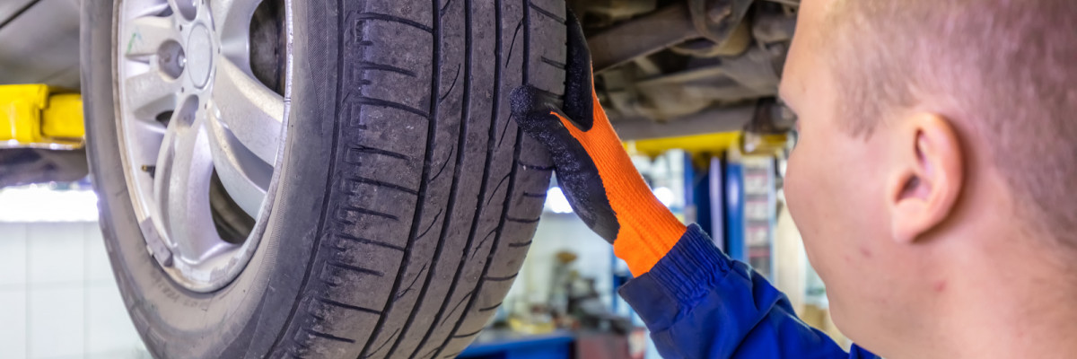 close-up-shot-of-mechanic-checking-very-attentively-surface-of-a-car-tire-mechanic-wearing-blue-coverall-and-orange-gloves-car-is-on-a-hydraulic-lift